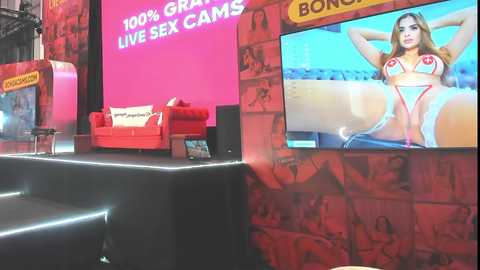Media: A video of a modern exhibition booth with a large screen displaying a woman in a red bikini, red walls, and a red couch.