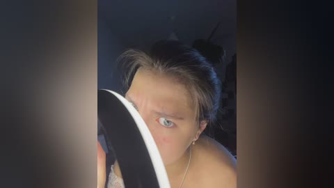 Video of a woman with light skin, brown hair, and blue eyes, partially hidden by a large black hat. She wears a delicate necklace and is seen from a close-up angle, suggesting intimacy and mystery.