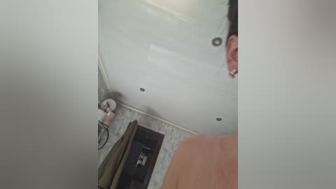 A video showing a white ceiling with a small, circular light fixture and a partially visible, nude person's shoulder and upper arm in a bathroom.