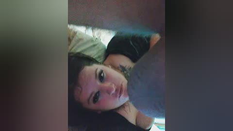 A video of a young woman with dark hair, wearing a black top, lying on her back, with a blurred, shadowy figure partially obscuring her face.