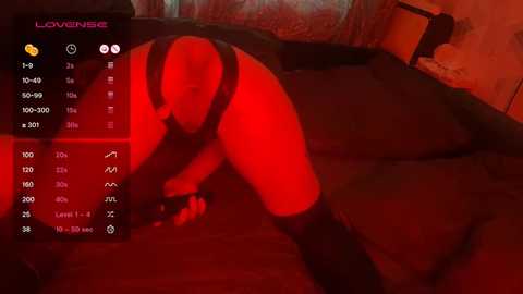 Video of a nude, light-skinned woman in a submissive pose on a bed, wearing only black thigh-high socks, with red lighting creating a sensual atmosphere.