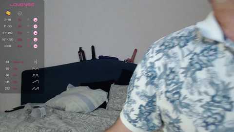 A video shows a person in a blue floral shirt, partially visible, standing near a neatly made bed with gray bedding and a black headboard. A digital calendar with dates and events is displayed on the left.