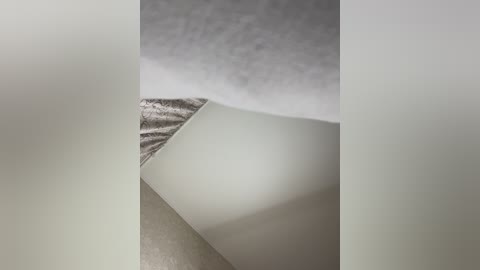 Media: Video of a white, textured wall with a slight crease, partially covered by a white, smooth, folded sheet of paper, creating a stark contrast of textures and colors.