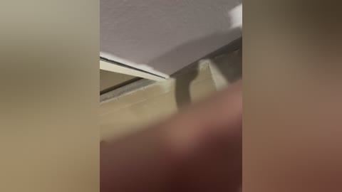 A blurry video of a beige wall with a white ceiling corner, showcasing a slightly textured surface and a faint shadow cast by an unseen object. The lighting is soft, creating a muted, unremarkable ambiance.