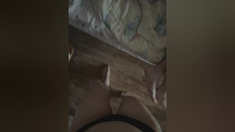 A dimly-lit video depicts a close-up view of a woman's legs and thighs, partially clad in black panties. The background shows a bed with a patterned quilt. The image is grainy, suggesting a low-quality video.