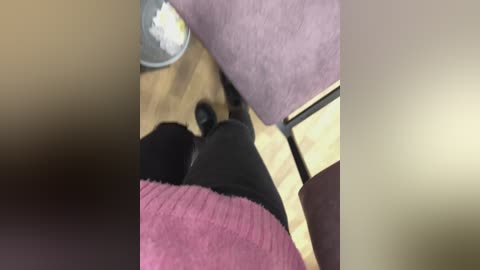 Video of a person wearing a pink sweater and black pants standing on a wooden floor, with a purple cushion and a metallic bowl visible in the background.