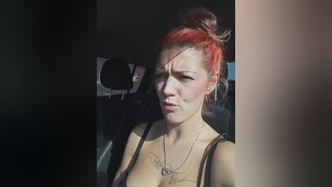 Video of a fair-skinned woman with red hair tied in a messy bun, wearing a black tank top, sitting in a car with dark interiors.