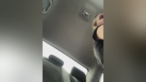 Video of a blonde woman wearing a black tank top, leaning forward in a car, seen from the driver's perspective.