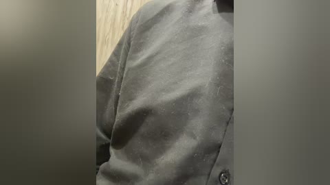 Media: A video of a person's upper torso wearing a grey, slightly wrinkled jacket, seen from the side, with blurred, neutral-colored background and visible light wooden texture.