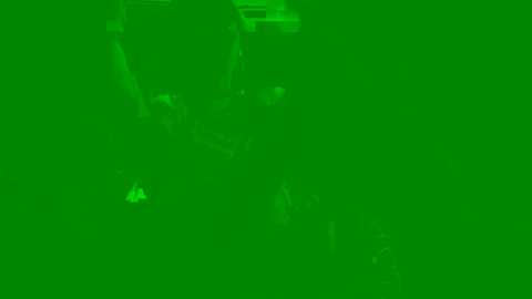 A green-tinted video with a blurred, indistinct figure in the background, possibly a person, standing near a building with visible architectural details. The image has a somewhat hazy, out-of-focus quality.