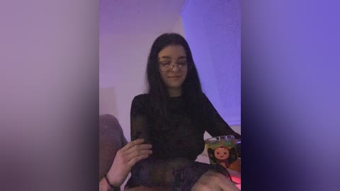 A young Asian woman with long black hair and glasses, wearing a sheer black top, sits in a dimly lit room with purple lighting. She holds a glass of juice.