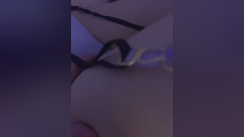 A dimly lit, close-up video of a woman's torso in black lingerie, with her breasts partially exposed. The image has a soft, intimate vibe with a purple hue.