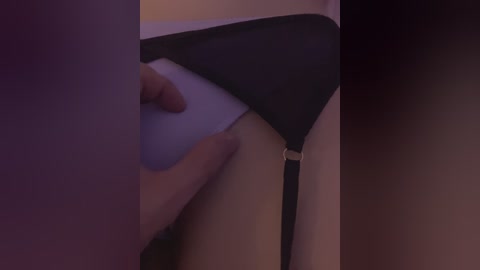 Video of a hand pulling down black panties revealing white underwear, blurred background with warm lighting.