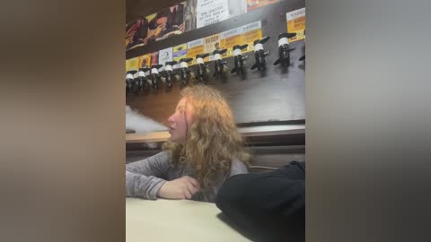 Media: A candid video shows a woman with long, curly blonde hair and a gray shirt, sitting in a restaurant booth. Behind her, a menu board displays various drink options. The setting is casual and brightly lit.