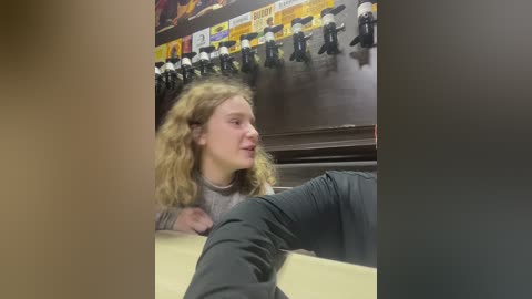 Media: Video of a blonde girl in a gray shirt, leaning on a counter, watching a marching band in a gymnasium with yellow banners.