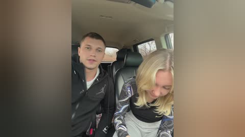 A video of a young blonde woman in a patterned jacket, sitting next to a young man in a black jacket, in a car.