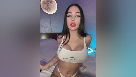 Media: Video of a young, light-skinned woman with long black hair, wearing a white crop top and matching thong, posing seductively on a bed. Moon-shaped light fixture in background.