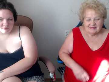 Video of two middle-aged women, one with curly hair, in a beige chair, the other with short hair, in a red dress, seated on a blue chair, in a plain room.