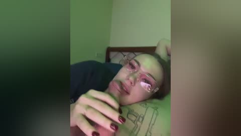 Video of a young woman with fair skin, wearing glasses, lying on a bed with a pillow, looking sad and with a bloody nose.