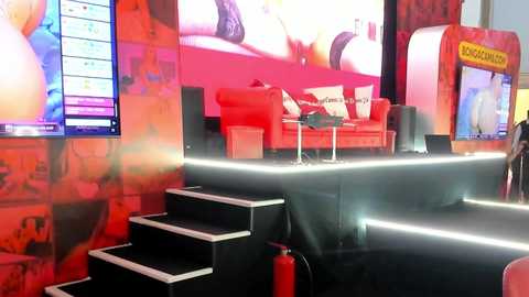Media: Video of a vibrant, modern bar interior with red walls, neon lighting, and a staircase leading to a stage with a DJ booth and a large screen displaying colorful visuals.