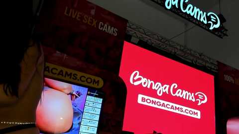 Media: Video of a crowded adult video store with multiple large screens displaying pornographic content, including a \"BongaCams\" advertisement.