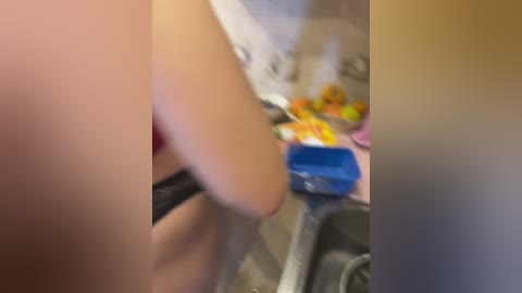 A blurry video showing a person's arm in a black top, holding a blue bag, with a kitchen background featuring a stove and a counter with food items.
