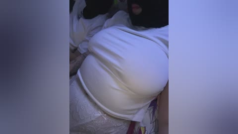 Video of a woman with a large, round belly and dark hair, partially obscured by a white shirt, lying on a bed.