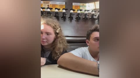 Media: A video of two young people in a fast-food restaurant, blurred due to motion. The girl has curly hair, wearing a black jacket, while the boy has short hair, wearing a white t-shirt.