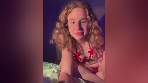 Media: Video of a fair-skinned, curly-haired woman in red lingerie, lying on a bed with green sheets, in a dimly lit room.