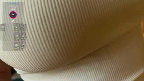 Video of a close-up of textured beige fabric with a waffle weave pattern. The background is blurred, with a digital overlay showing statistical data and a pink circular logo.