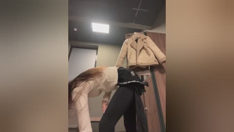 Media: Video of a person in a beige jacket and black leggings bending over to put on a beige jacket and a black skirt with white stripes.