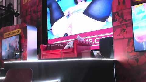 Media: Video of a vibrant, colorful booth at a convention featuring a large, animated video screen, red couches, and posters.