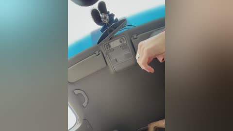 Media: Video of a woman's hand adjusting a microphone on a car dashboard, with a blue sky visible through the windshield.