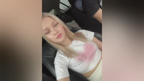 Media: Video of a young, blonde woman with light skin, wearing a white T-shirt and beige shorts, reclining in a black car seat, eyes closed, possibly asleep.