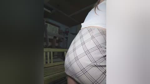 A video showing a woman's bare buttocks clad in a plaid skirt, standing in a dimly lit, cluttered room with a yellow bunk bed and miscellaneous items in the background.