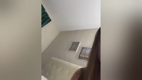 Media: A video of a simple, sparsely furnished room with a beige ceiling, a wooden bed, a green curtain, and two framed pictures on a light beige wall.