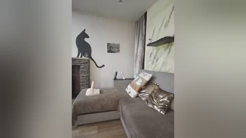Media: Video of a modern, minimalist bedroom with a grey sofa, abstract wall art, and a black silhouette of a cat on a stone pillar.