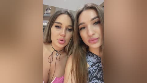 Media: Video of two young women with long, straight, light brown hair, wearing makeup, standing close together. One in pink, the other in black snake print, kissing each other.