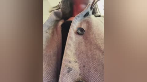 Media: A close-up video of a person wearing a beige and grey houndstooth-patterned jacket over a black shirt, with a visible red spot on the chest. The background is blurred, and the image focuses on the neck and shoulders.