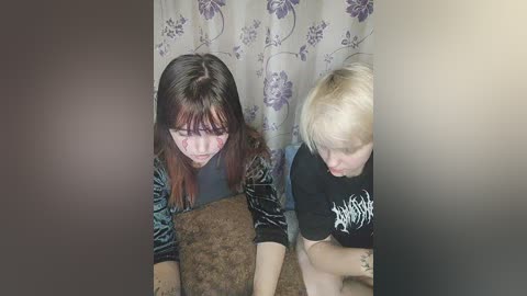 Media: Video of two women with long hair, one with a tattoo, sitting on a brown couch; the woman on the right has blonde hair and wears a black shirt.