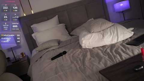 Video of a dimly lit hotel room with a king-sized bed, two pillows, and a gray comforter, featuring a digital clock and remote control on the nightstand.