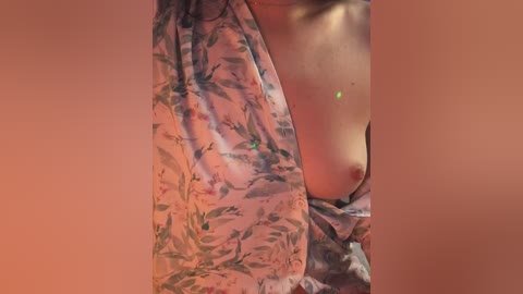 Media: A video of a light-skinned woman wearing a floral-patterned, sheer robe, revealing her bare chest and nipple. The background is a warm, peach-toned wall.