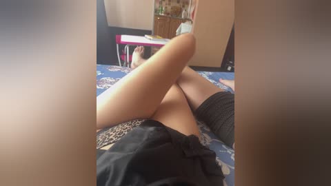 Video of a woman lying on her back on a bed with leopard-print sheets, wearing black shorts and black thigh-high socks. The room has a wooden dresser and a red table.