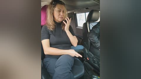 Media: A video of a light-skinned woman with shoulder-length brown hair in a black turtleneck and pants, seated in a taxi with a pink cushion behind her.