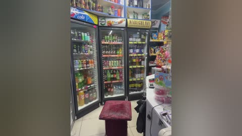 Media: Video of a small, brightly lit convenience store with three glass refrigerators filled with drinks. A red bench sits in the middle, and shelves display various snacks and beverages.