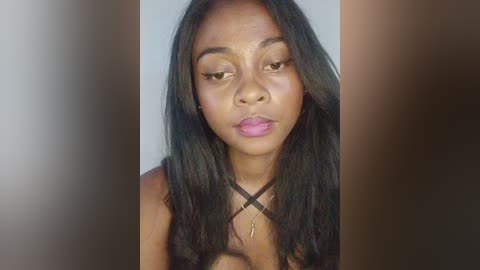 Video of a young African-American woman with long, wavy black hair, wearing a black cross necklace, looking serious with a slight pout, set against a blurred background.