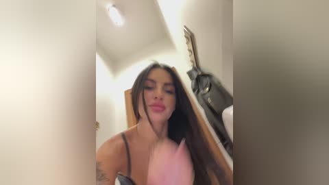 Media: A video of a young woman with long dark hair, wearing a pink bra, posing in a dimly lit bathroom with a towel hanging on a wooden door.