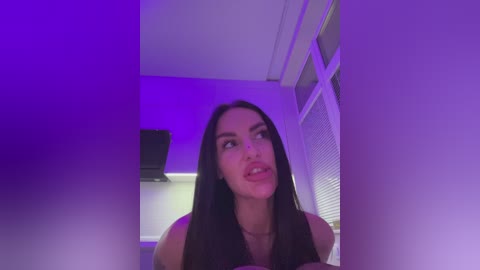 Media: A video of a woman with long black hair, wearing a black top, standing in a room with purple lighting.