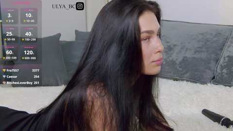 Video of a long-haired, fair-skinned woman lying on a gray couch in a modern living room.
