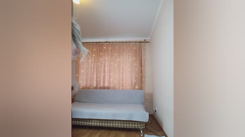 Video of a small, cozy room with a light pink wall, beige curtains adorned with golden stars, and a white couch with a checkered pattern.